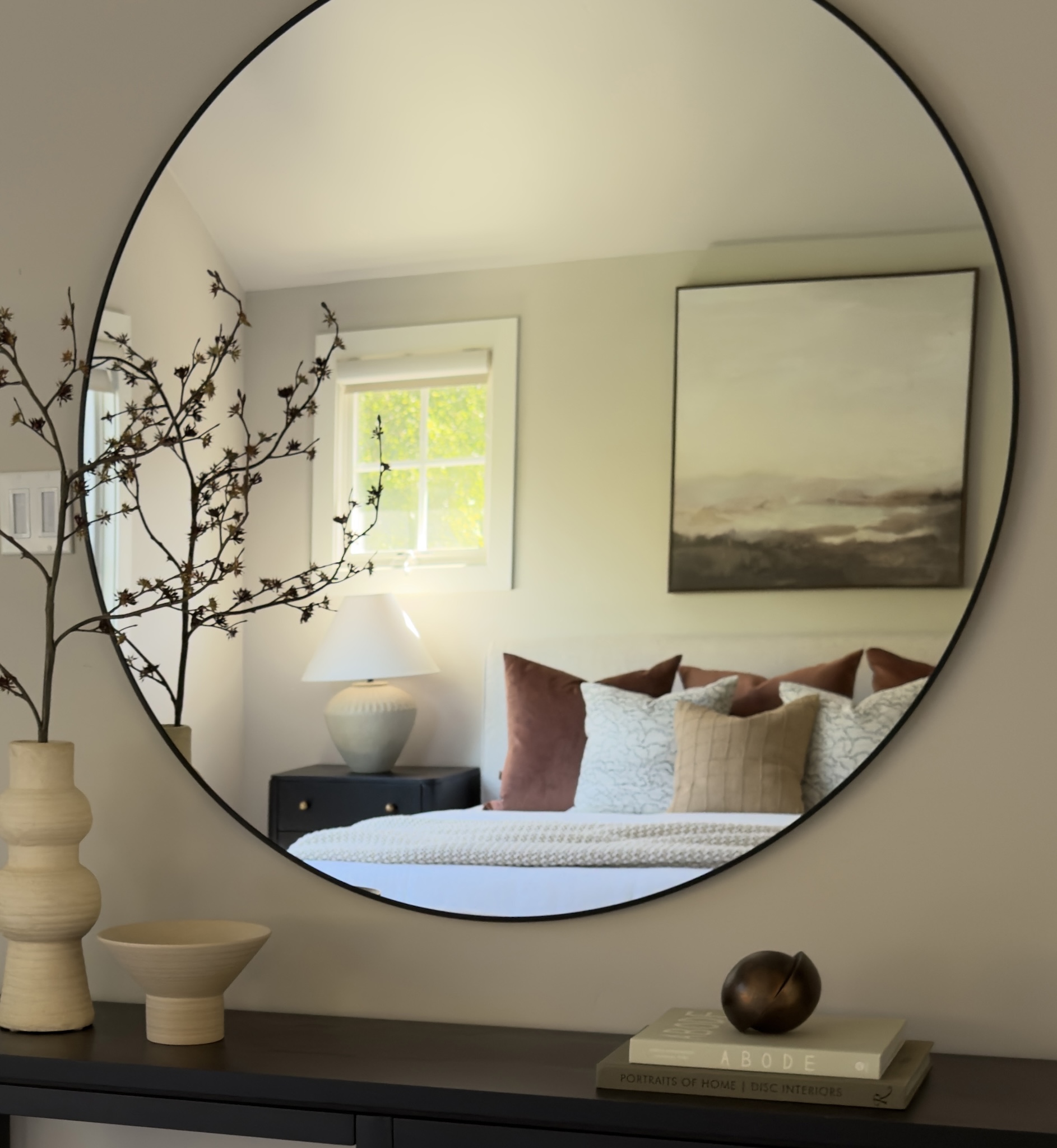 Round mirror reflecting the staged primary bedroom
